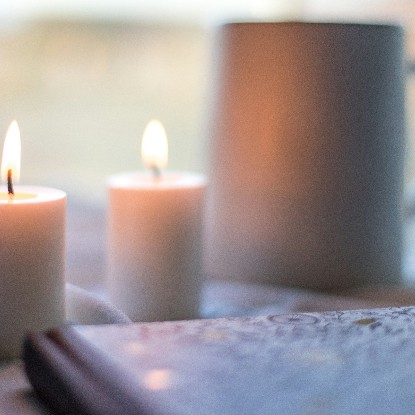 Lit candles burning beside a mug and an open book in soft window light
